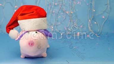 软玩具粉红色的猪在蓝色背景上戴着红色圣诞老人帽子，新年灯和罐头，2019年的<strong>猪年</strong>。